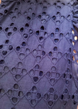 Close-up of a navy blue eyelet lace top with a textured diamond pattern and ruffled sleeves.