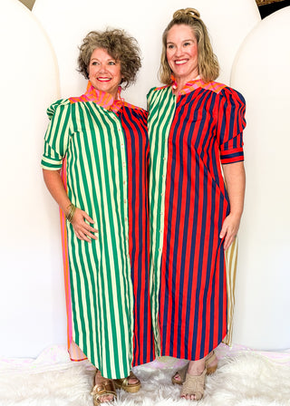 Two women standing side by side wearing matching midi dresses with vertical stripes. The dress on the left has green and white stripes with orange trim, and the dress on the right has red and navy blue stripes with orange trim.