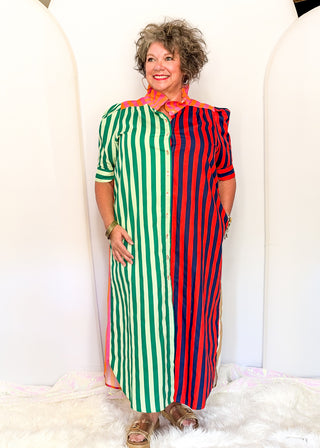 A woman modeling a long-sleeve midi dress with a vertical stripe pattern split down the middle: green and white stripes on the left, red and white stripes on the right, with a bright orange collar.