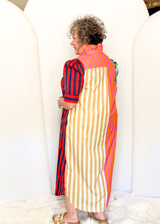 A woman wearing a colorful striped midi dress, photographed from the back in a studio setting with white arched backdrops.