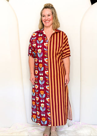 A woman modeling a long, short-sleeved tunic dress with a split design: one side features a red background with colorful floral and butterfly patterns, and the other side has vertical red and orange stripes.