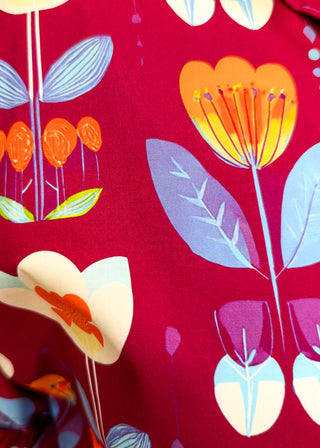 A close-up of a red fabric with a retro floral pattern featuring orange, yellow, light blue, and white flowers.