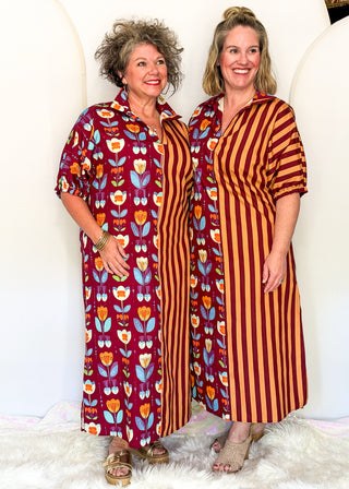 Two women modeling matching long button-front dresses with contrasting prints. The dress on the left features a burgundy base with a colorful floral pattern in orange, yellow, and blue.