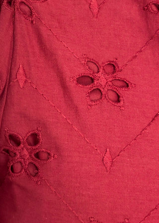 A close-up of a red fabric with embroidered floral eyelet patterns and stitched diagonal lines.