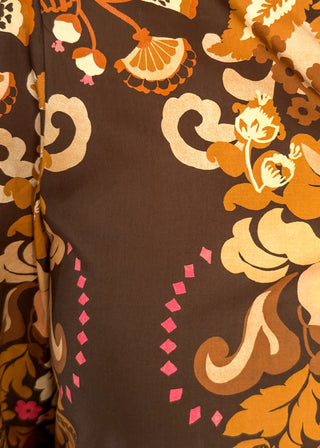 A close-up of a brown fabric with a retro floral and scroll pattern in orange, beige, and pink.