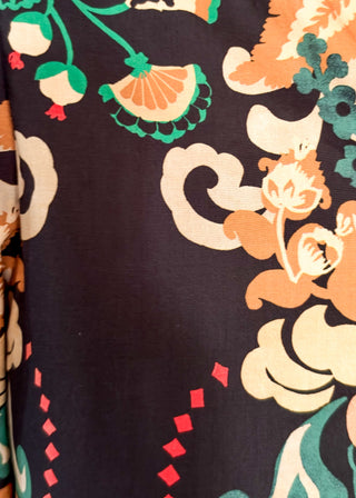 A close-up of a fabric pattern featuring stylized floral and cloud-like motifs in orange, cream, green, and red on a very dark charcoal background.