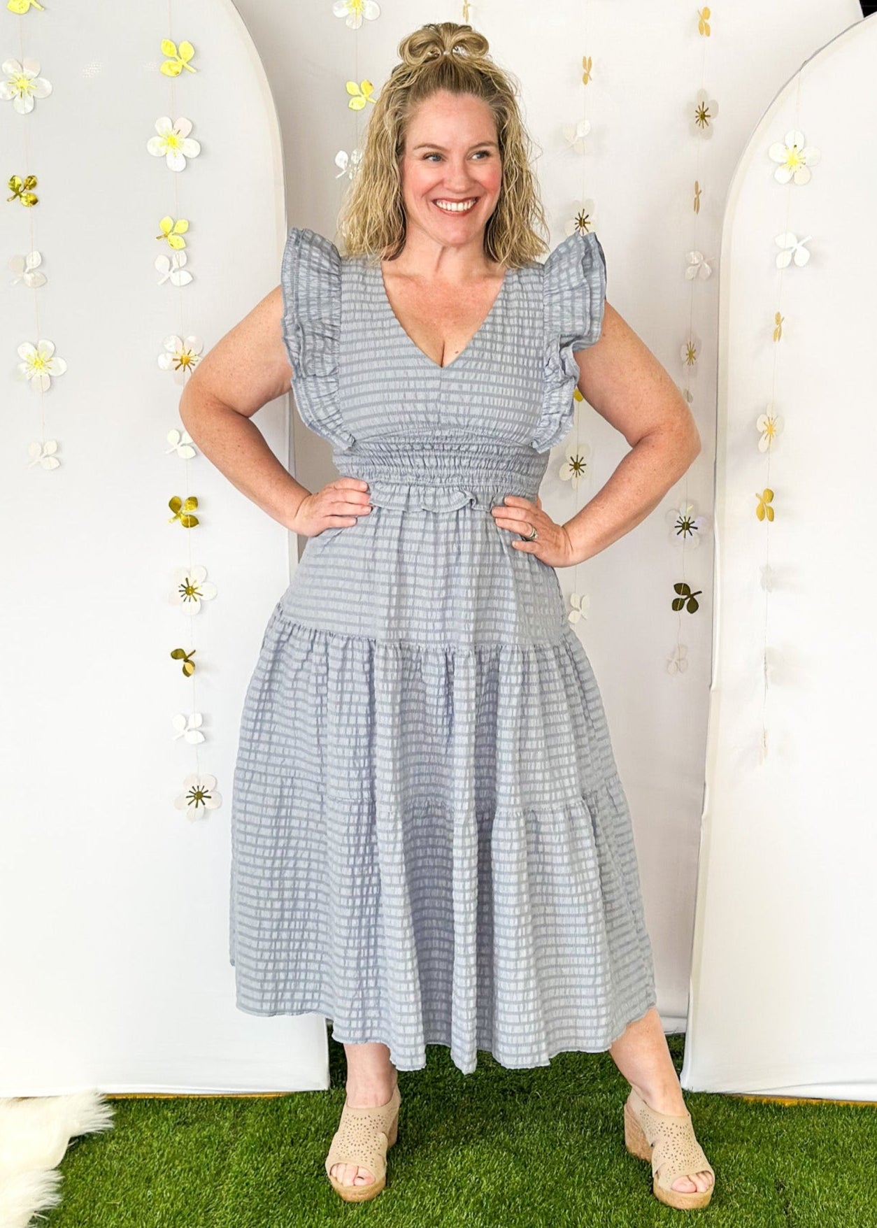 Flutter sleeve, V-neck tiered dress-ruffle detail at waist. Solid color in a blue-gray with seersucker like texture. 