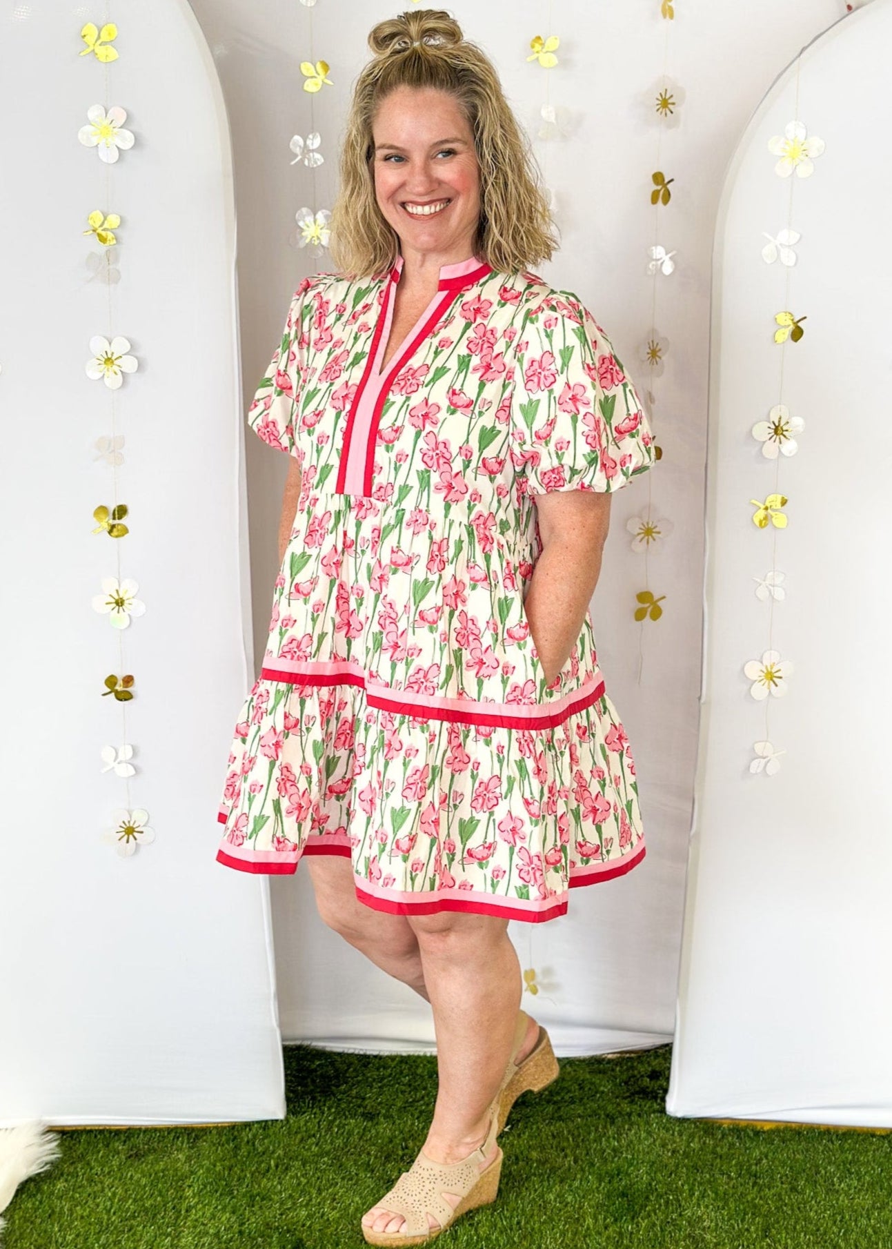 Cream base with pink wildflowers.  pink and dark pink ribbon detail on v-neck, collar, and around the bottom tier.  Puff sleeve-lined;with pockets. 