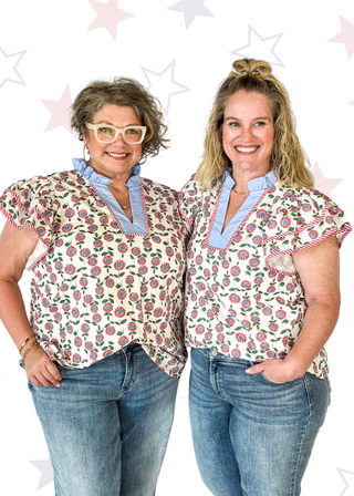 red and blue flowers with green stems on a cream background double ruffle short sleeve top - v-neck - light blue band around ruffle collar and v-neck - candy strip red and white piping detail around double ruffle short sleeves and v-neck
