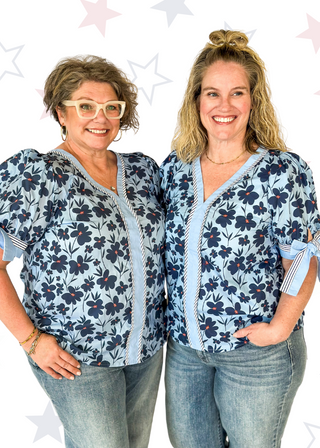 light blue top with navy flowers and red centers - light blue band around v-neck and straight down the front with blue and white striped trim along side it - light blue and striped bow at cuff
