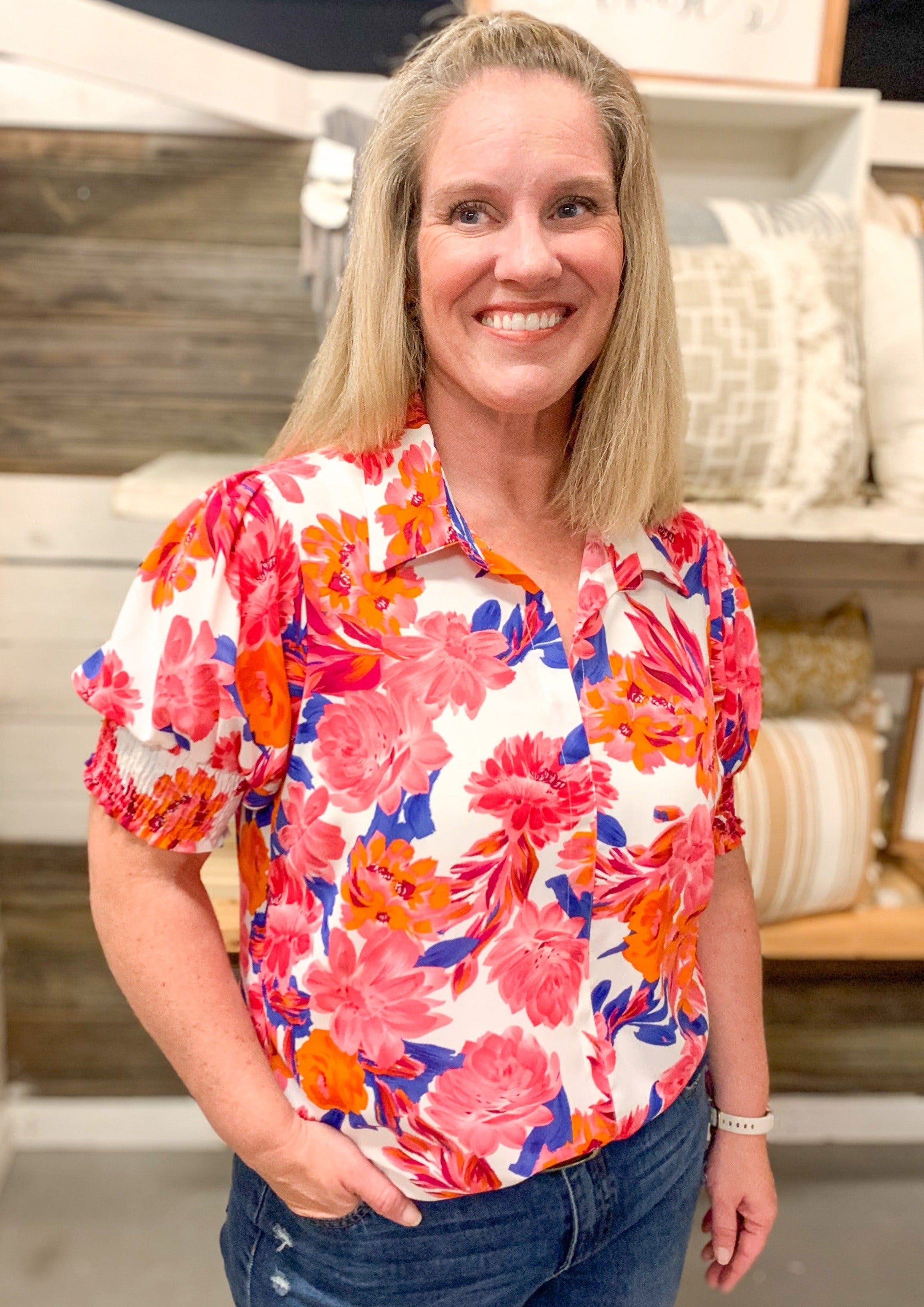 White top with V neckline, collar, and seem down the middle. Floral pattern is made up of Fuchsia, orange, and blue.