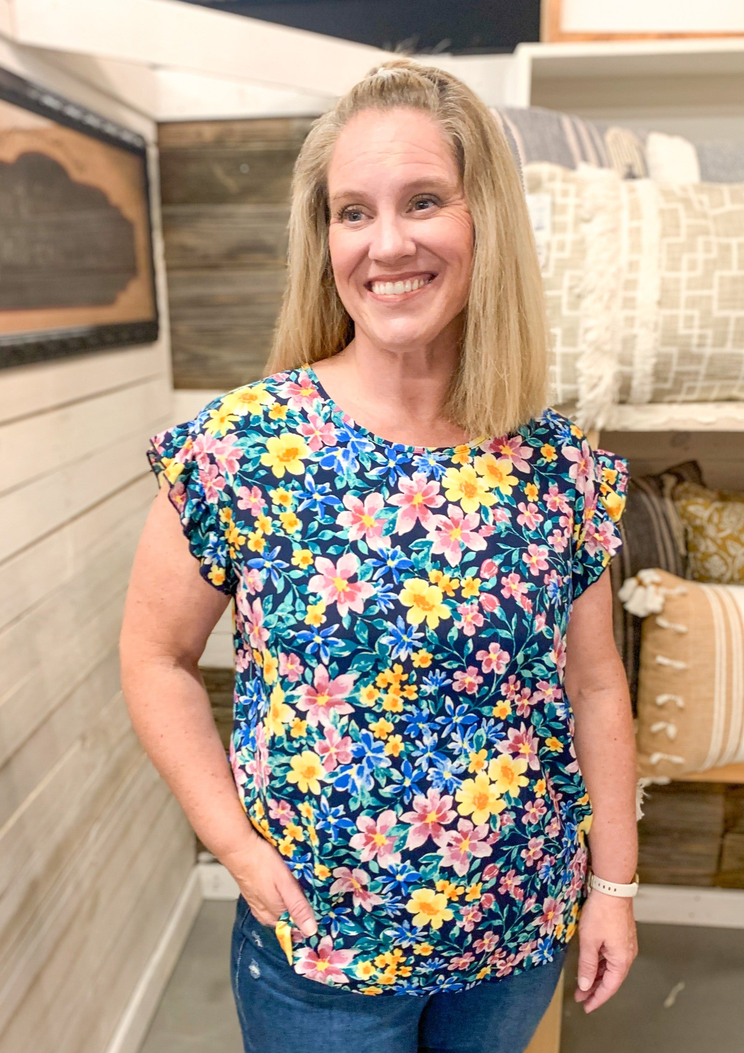 Navy top with ruffle sleeve detail with a fun floral pattern. Colors include pinks, yellows, blues, and greens.