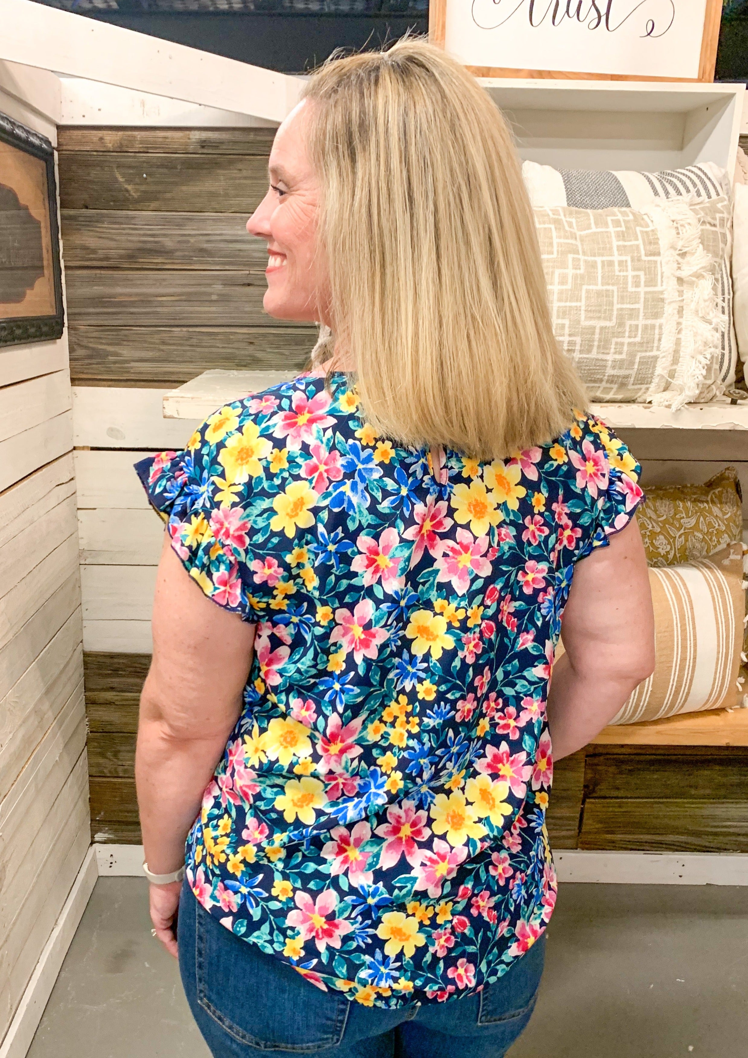 back of Navy top with ruffle sleeve detail with a fun floral pattern. Colors include pinks, yellows, blues, and greens.